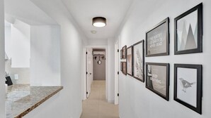 A hallway with a marble countertop, a ceiling light, and framed artwork on the walls. - Modern Beachside 2BR | Steps to Beach + Heated Pool (Pompano Beach)