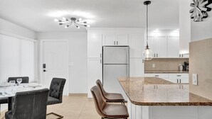 A modern kitchen with white cabinets, a granite countertop, and a built-in refrigerator. - Modern Beachside 2BR | Steps to Beach + Heated Pool (Pompano Beach)