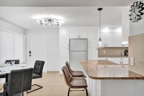 A modern kitchen with white cabinets, a granite countertop, and a built-in refrigerator.