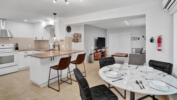 A modern kitchen with a central island, dining area with a round table, and a living space with a sofa. - Modern Beachside 2BR | Steps to Beach + Heated Pool (Pompano Beach)
