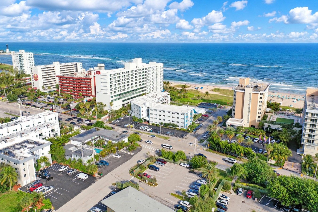 A coastal cityscape with a beachfront hotel, parking areas, and a clear view of the ocean.