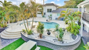 A swimming pool with a curved design, surrounded by palm trees and a stone deck. - Modern 1BR Beachside | Heated Pool + Parking (Pompano Beach)