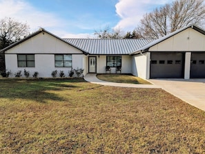 Une maison moderne à deux étages, dotée d’un garage, d’une pelouse devant et d’un petit patio.