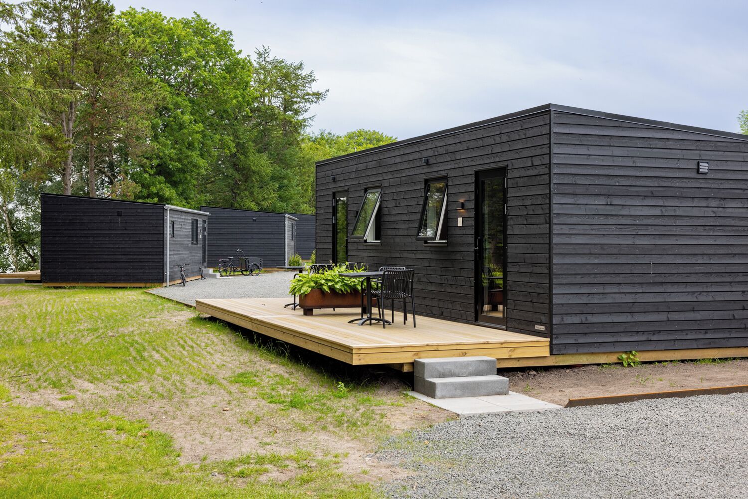 Een moderne, donkere hut met een houten terras en een zitgedeelte buiten.