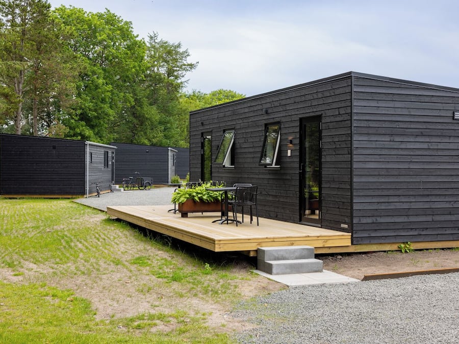 A modern, dark-colored cabin with a wooden deck and outdoor seating area.