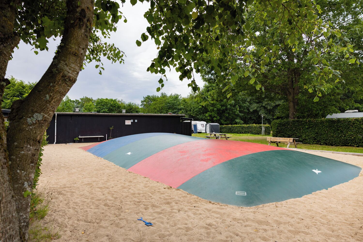 A sandy outdoor area with a multi-colored play surface and a black building in the background.