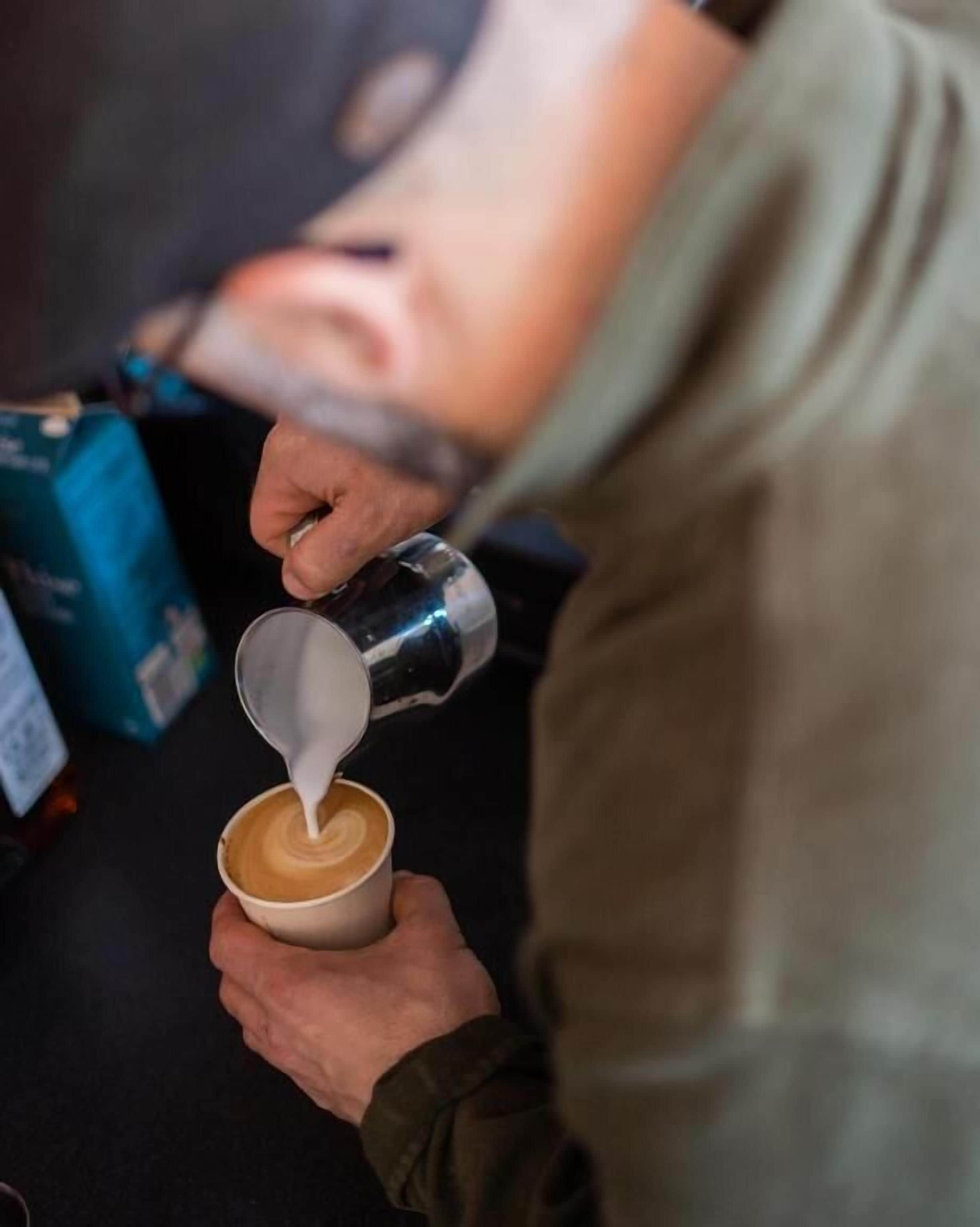 Una persona vertiendo leche en una taza de café.