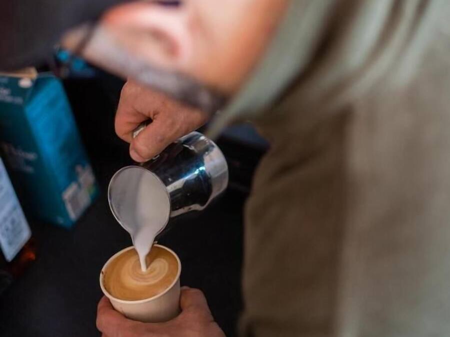 Una persona vertiendo leche en una taza de café.