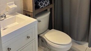 Un baño con un lavabo blanco, un inodoro, un armario de madera con un marco de foto y una cortina de ducha.