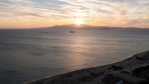 A coastal sunset view with calm sea, distant mountains, and a beach with parked cars. - VILLA KERAMEAS PLAKA NAXOS (Plaka)