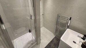 Et moderne badeværelse med en glasbrusekabine, en hvid vask og et håndklædestativ.
