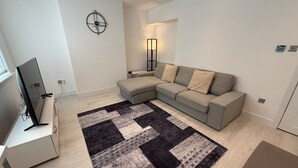 En moderne stue med en modulsofa, et fladskærms-tv, et gulvtæppe med mønster og et vægur.