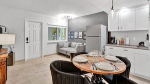 A modern kitchen with white cabinets, a built-in refrigerator, a dining table set for four, and a gray sofa in the living area.