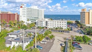 A coastal hotel with multiple floors, a parking lot, and a view of the ocean.