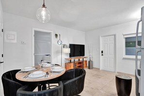 A dining area with a round table set for four, a television, and a door leading to another room.