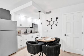 A modern kitchen with white cabinets, a built-in microwave, and a dining area with a round table and four chairs.