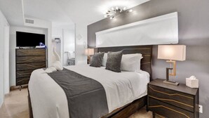 A modern hotel room with a large bed, bedside tables, a TV, and a wall-mounted light fixture.