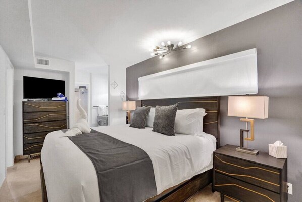A modern hotel room with a large bed, bedside tables, a TV, and a wall-mounted light fixture.