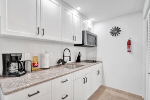 A modern kitchen with white cabinets, a granite countertop, a coffee maker, a microwave, and a fire extinguisher.