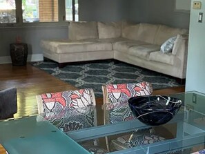 Una sala de estar con un sofá seccional color beige, sillones estampados, una mesa de centro de vidrio y un cuenco decorativo.