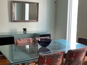 Un comedor con mesa de vidrio, sillas estampadas, un cuenco decorativo y un espejo en la pared.