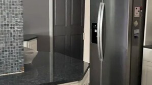 Una cocina con refrigerador de acero inoxidable, gabinetes blancos y encimera negra.