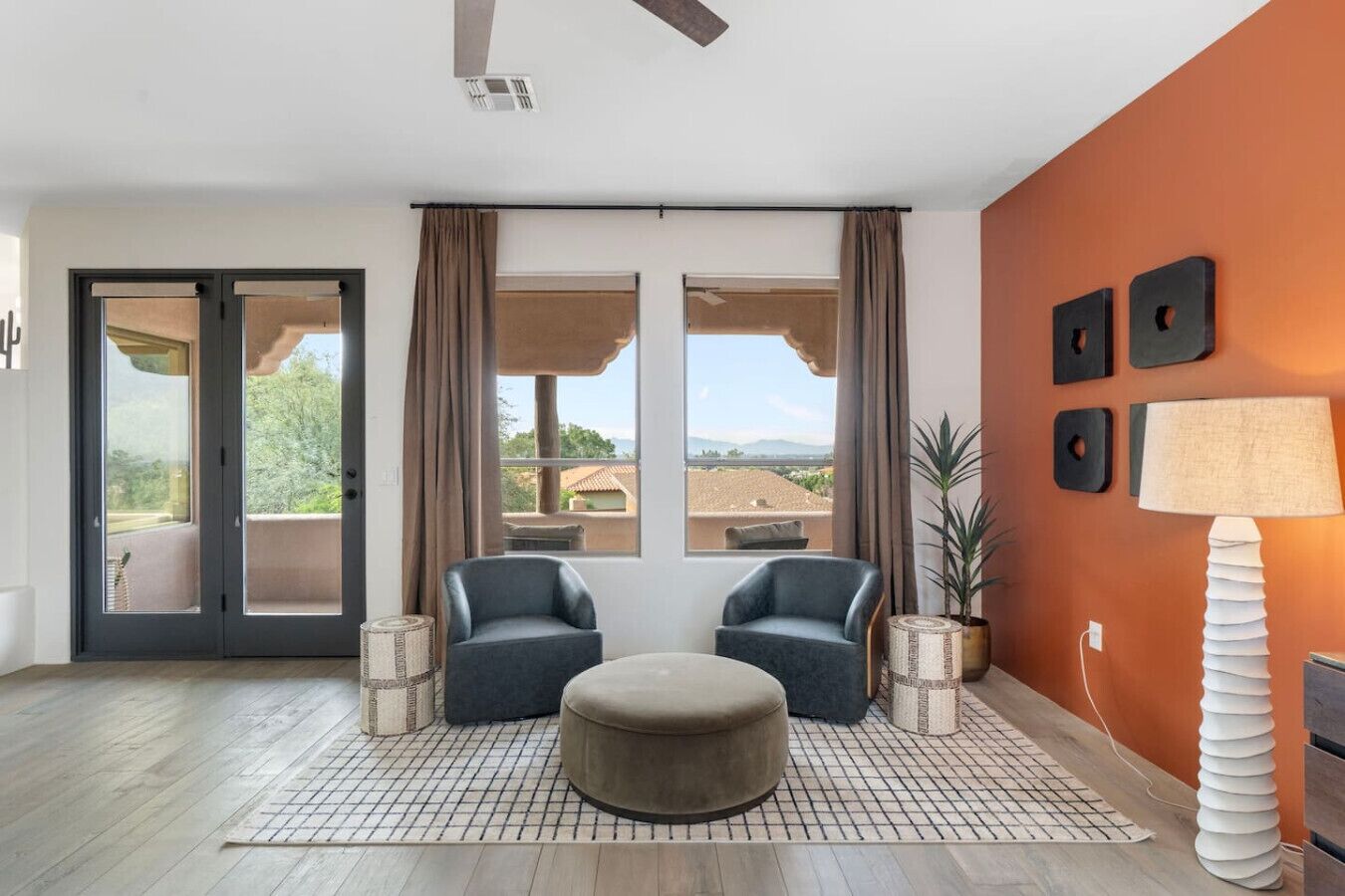 Un salon moderne avec deux fauteuils, un pouf rond, une lampe sur pied et une vue sur l’extérieur grâce à de grandes fenêtres.