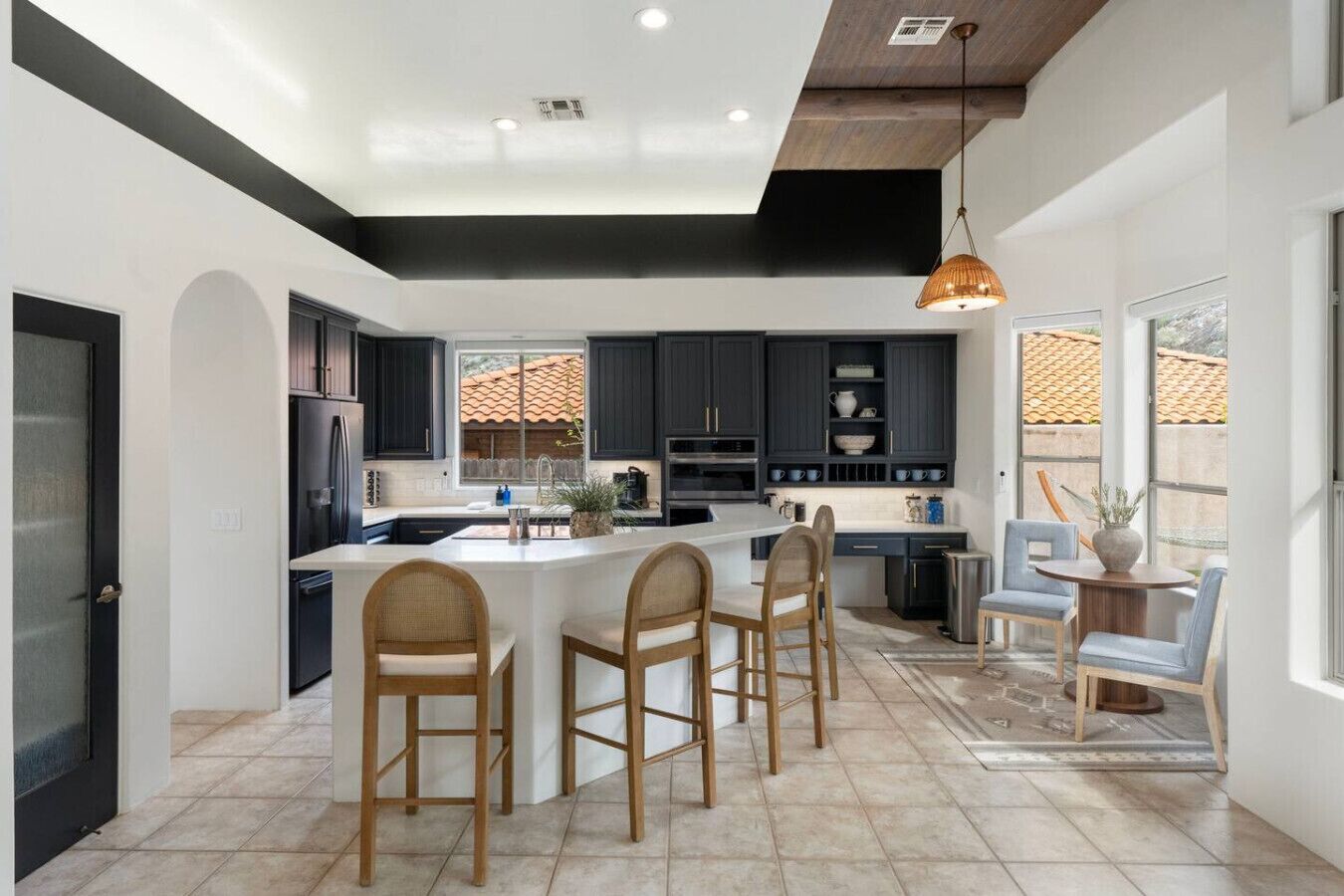 A modern kitchen with dark cabinets, a central island, and a dining area with chairs.