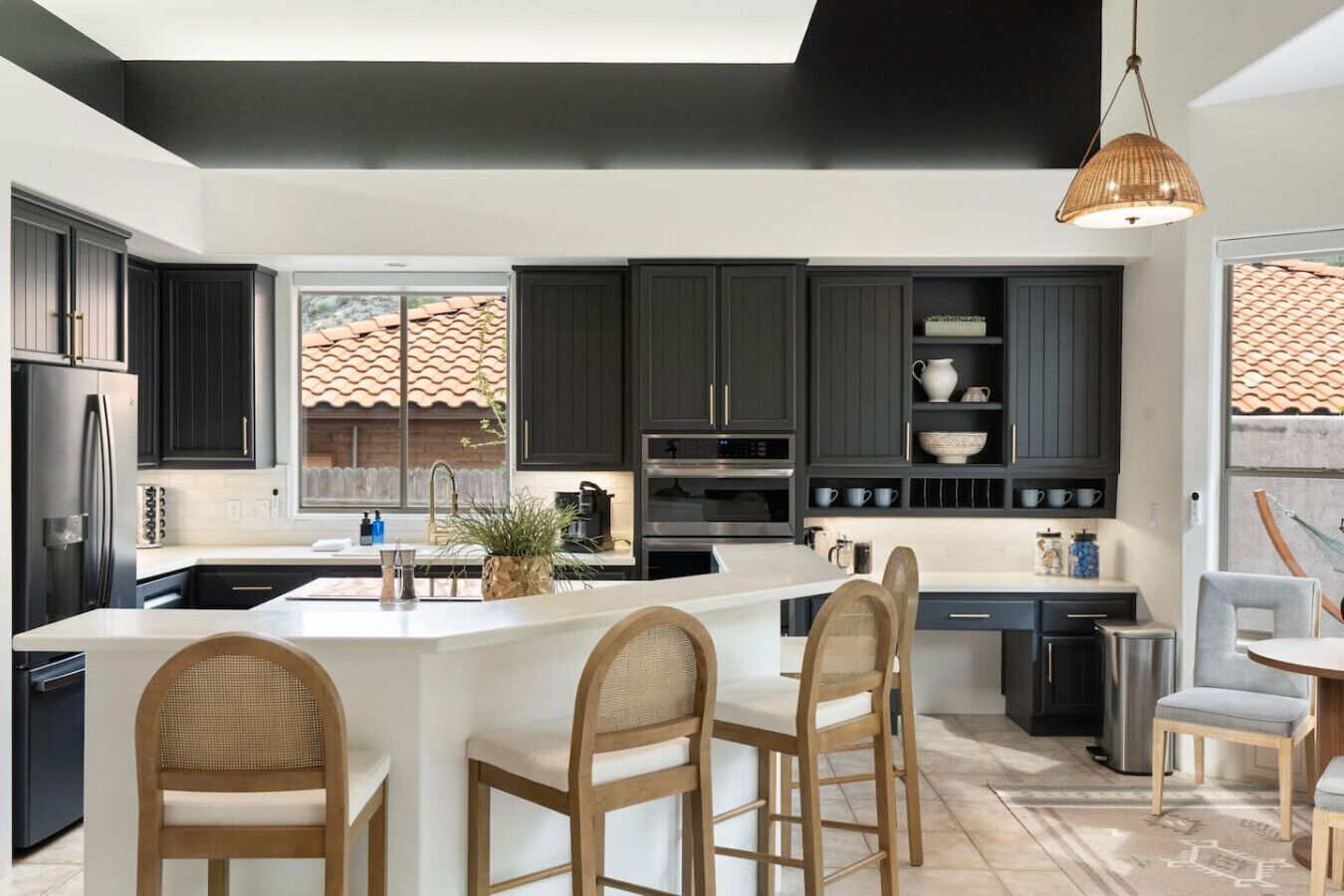 A modern kitchen with dark cabinets, a large island with bar stools, and a hanging light fixture.