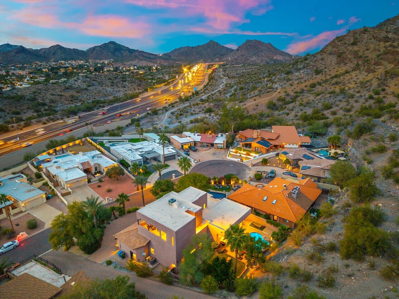 An aerial view of a residential area with houses, a road, and mountains in the background.