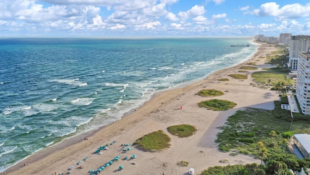Ein Strand mit Blick auf den Ozean, ein sandiger Uferstreifen und eine Reihe von Gebäuden.
