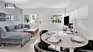 Ein modernes Wohnzimmer mit einem grauen Sofa, einem Couchtisch und einem Essbereich mit rundem Tisch, gedeckt für vier Personen.