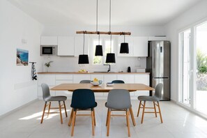 A modern kitchen with white cabinets, a wooden dining table, and four chairs. - Villa Aura Kastraki NAXOS (Kastraki)