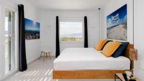 Ein Schlafzimmer mit einem großen Bett, Blick ins Freie, einem Sessel und Bildern an den Wänden.