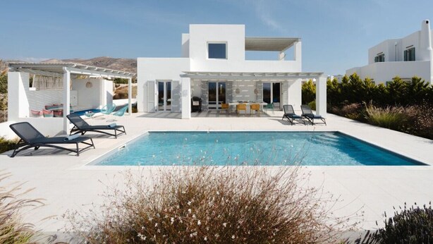 Eine moderne, weiße Villa mit Pool, Sitzgelegenheiten im Freien und einer überdachten Terrasse.