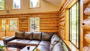 A log cabin interior with a leather sofa, large windows, and a view of trees. - Rebels Retreat-Minutes from Main St, Longtime Guest Favorite now with IronStone! (Ouray)