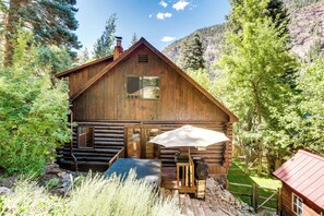 A rustic log cabin with a wooden deck, a grill, and a large umbrella.