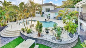 Ein Pool mit geschwungener Form, umgeben von Palmen und einer Stegterrasse.