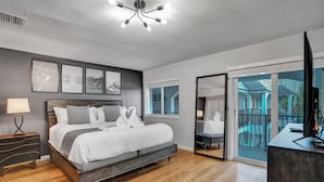 Ein modernes Schlafzimmer mit einem großen Bett, Nachttischen, einem Schreibtisch und einem Balkon mit Blick auf einen Pool.