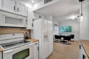A modern kitchen with white cabinetry, a built-in oven, and a dining area with a table and chairs. - Beach Retreat | 2BR + Heated Pool + Parking (Pompano Beach)
