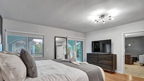 Ein modernes Schlafzimmer mit einem großen Bett, einem Schminktisch, einem Fernseher und einer Glastür, die auf einen Balkon führt.