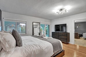 Ein modernes Schlafzimmer mit einem großen Bett, einem Schminktisch, einem Fernseher und einer Glastür, die auf einen Balkon führt.