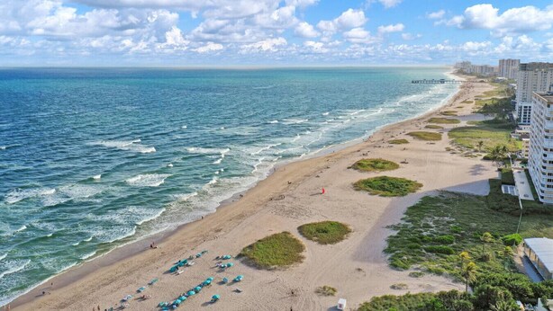 Ein Strand mit Blick auf den Ozean, ein sandiger Uferstreifen und eine Reihe von Gebäuden.