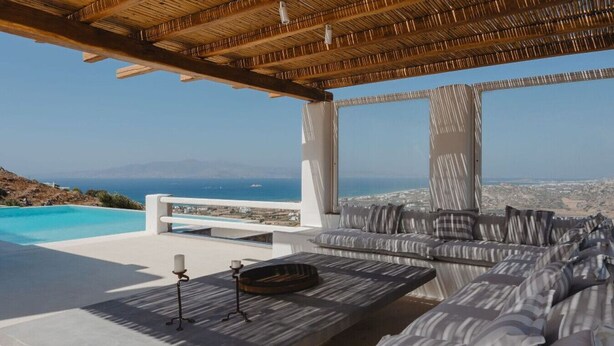 A modern outdoor lounge with a pool, a sofa, and a view of the sea and cityscape. - BLUE EYES VILLA Naxos Cyclades Greece (Naxos)