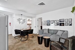 A modern living room with a gray sofa, black chairs, and a dining table. - 2BR Beach Escape | Heated Pool + Parking (Pompano Beach)