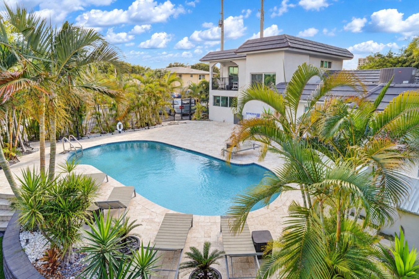 A swimming pool surrounded by palm trees and a two-story building with a balcony.