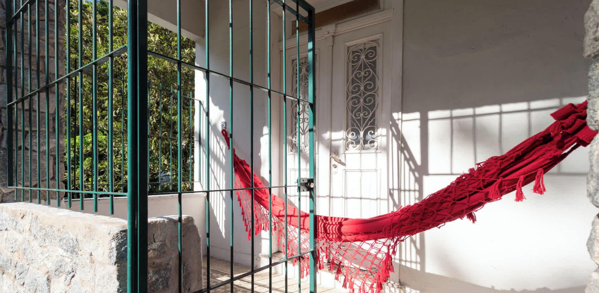 A hammock tied between metal bars, a white door with decorative metalwork, and a stone wall.