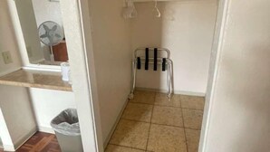 Un pasillo estrecho con piso de baldosas, un pequeño estante metálico y un bote de basura.