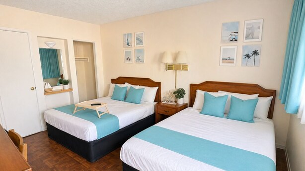 Habitación de hotel con dos camas, un aparador de madera, un espejo, una ventana con cortinas y decoración en la pared.