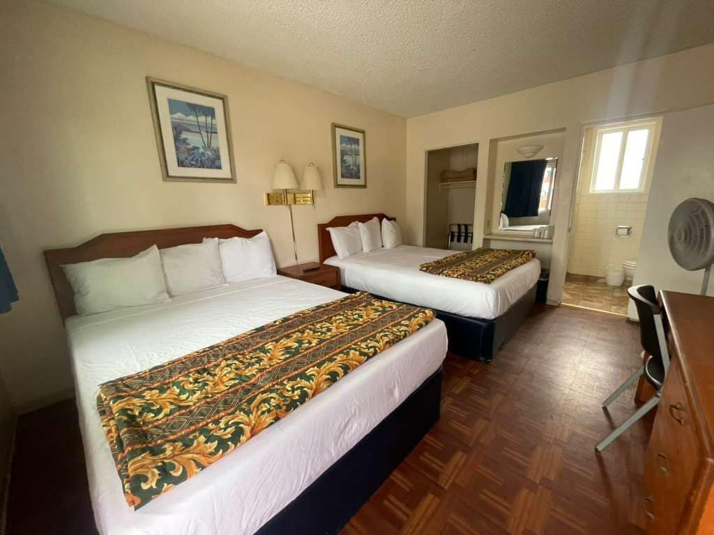 A hotel room with two beds, a desk, a chair, a wardrobe, and a window.